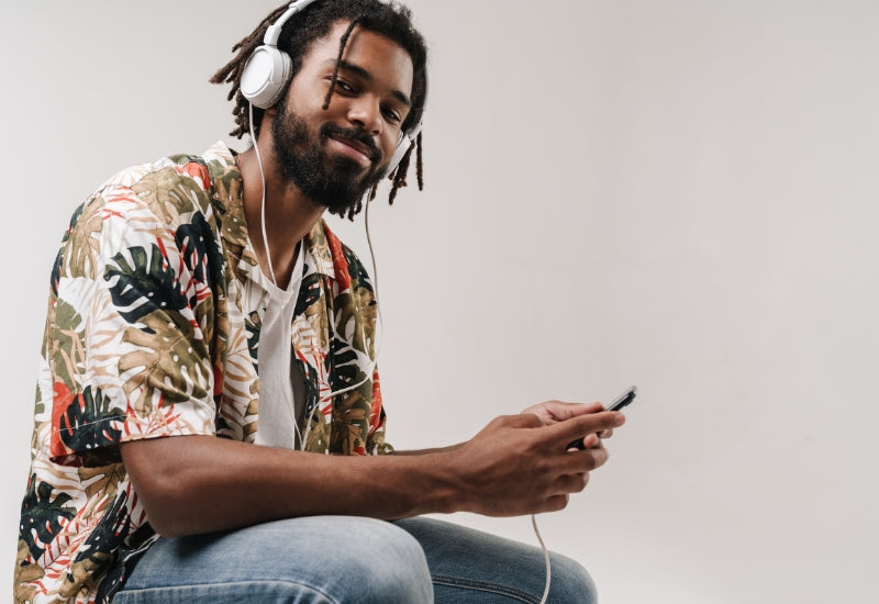 cool, content, youthful man with microlocs wearing headphones and holding a smartphone