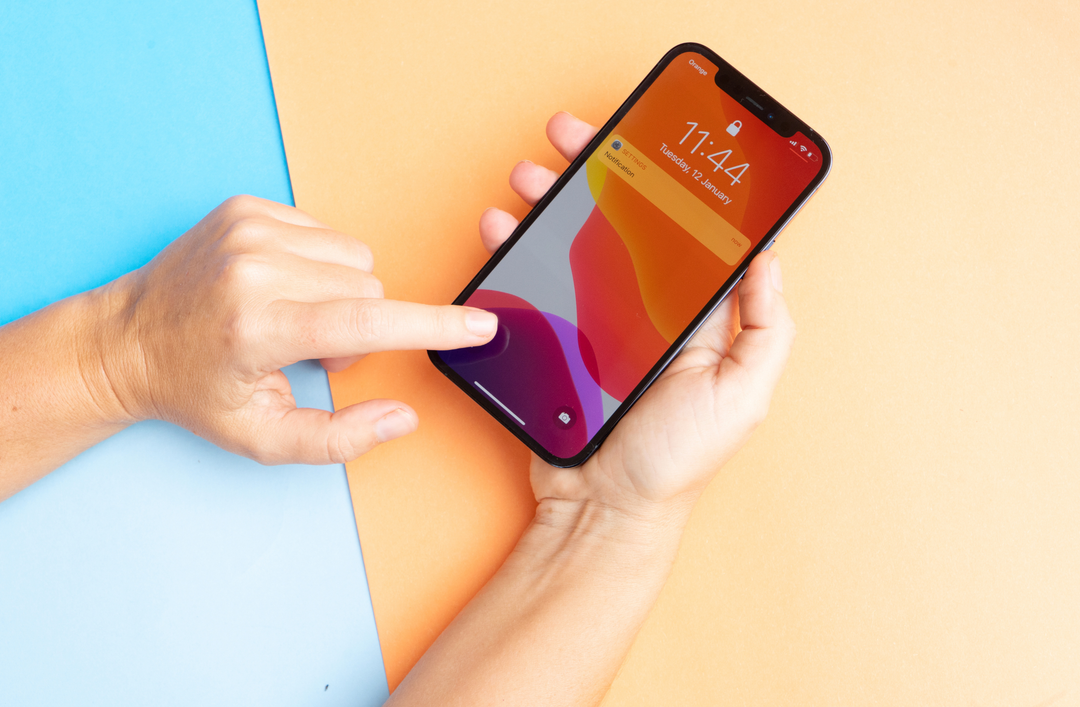 A person holding an iPhone with a vibrant lock screen against a blue and yellow background, highlighting the hardware and screen responsiveness testing.