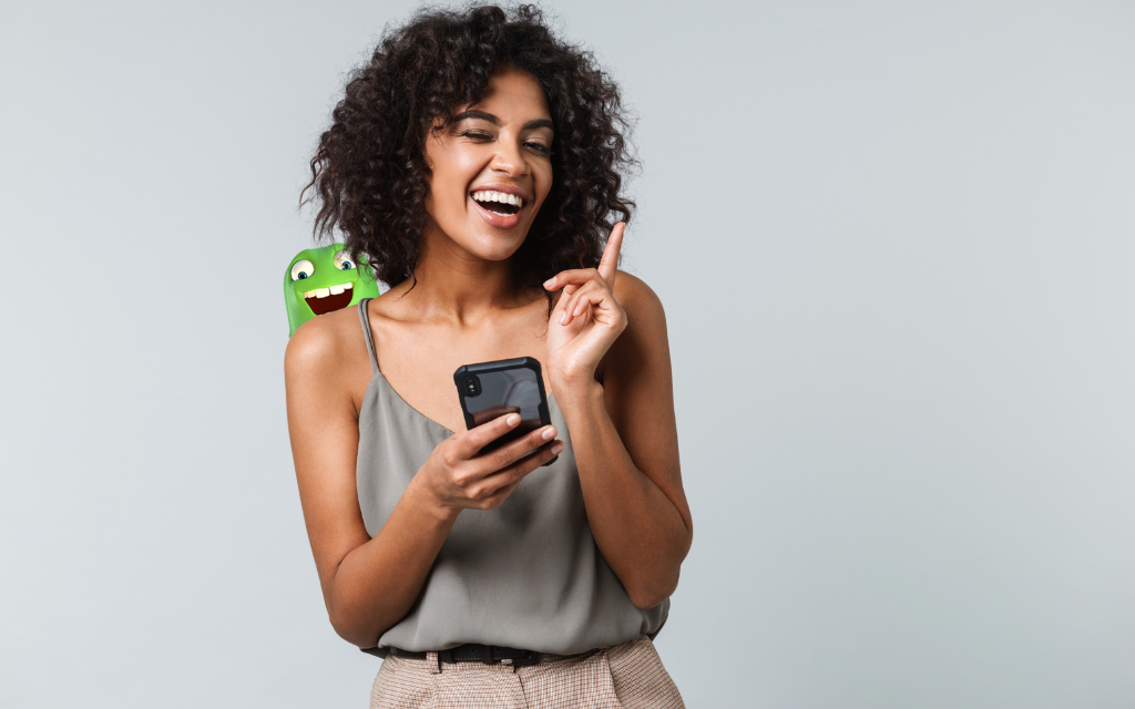 woman with black curly hair holding an iPhone with the little green Mobile Monster peaking over her shoulder