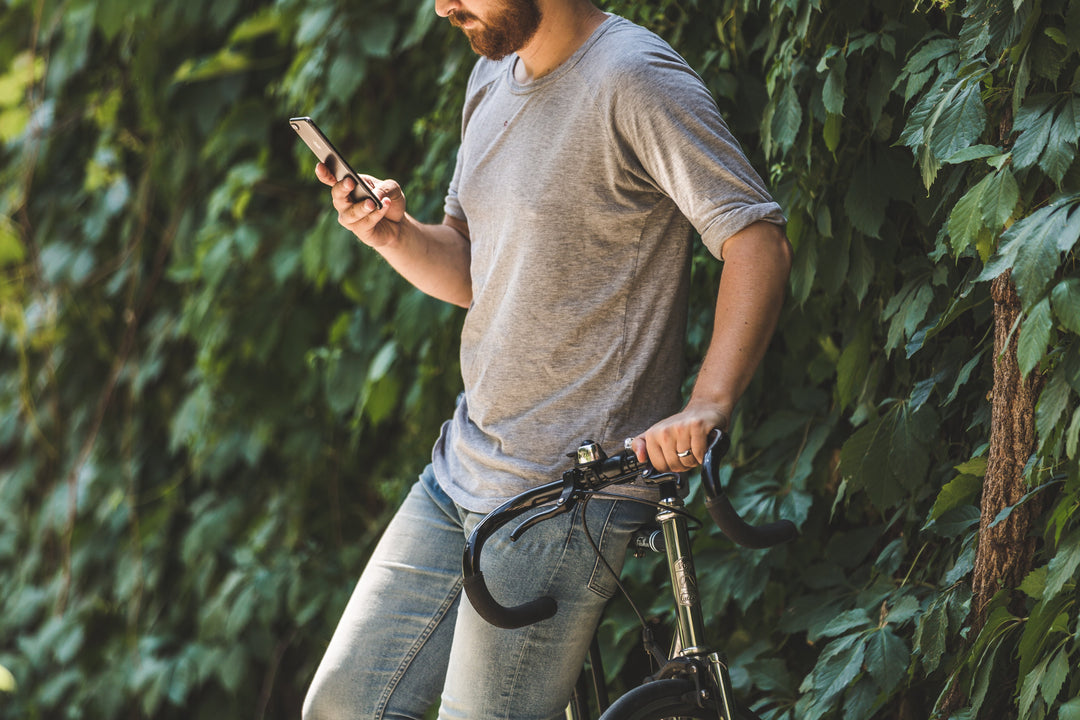 Guy leaning on a bicycle with an iPhone against a green plant wall