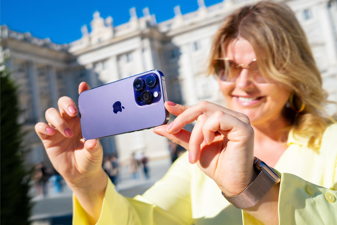 A woman smiling while using a purple iPhone 14 Pro to take a photo of a historic building.